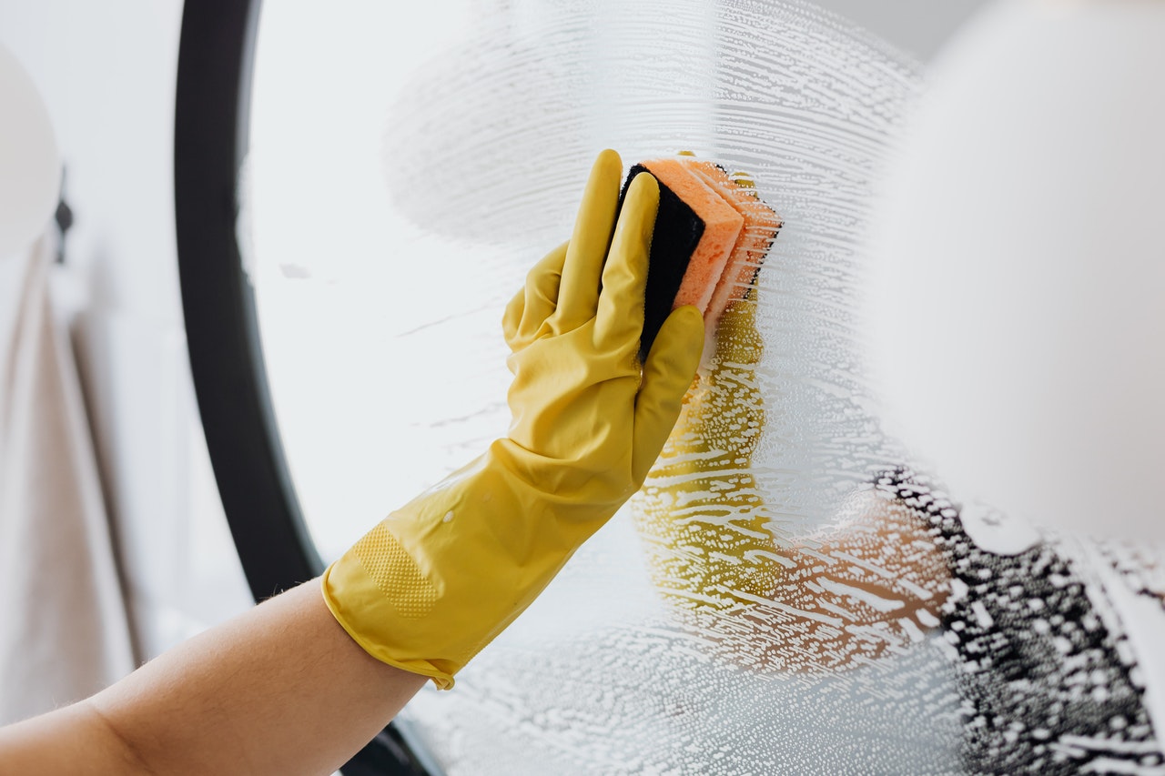 A person with yellow rubber gloves cleaning a mirror.