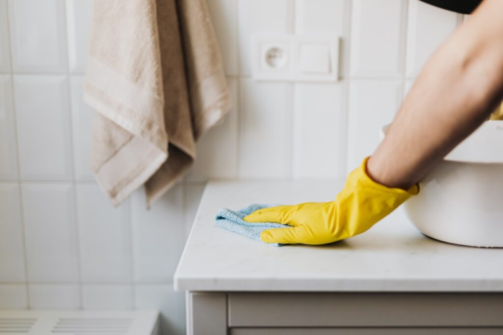 A person with yellow rubber gloves wiping down a counter in the bathroom.