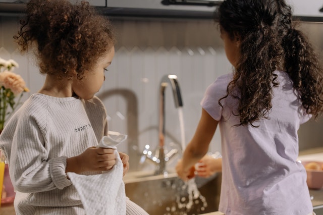 Two little girls washing the dishes and keeping a clean house.