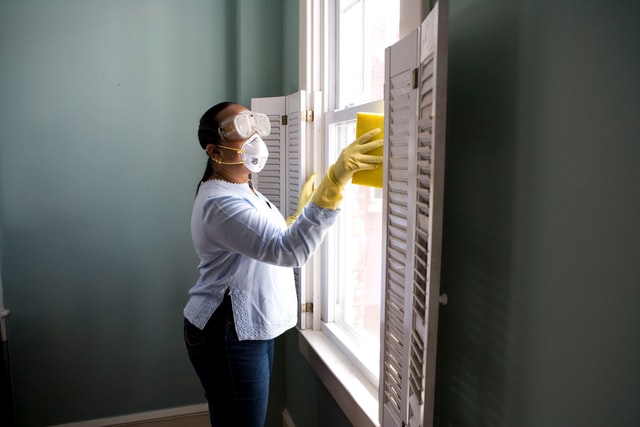 A professional cleaner washing windows in a room with gray walls