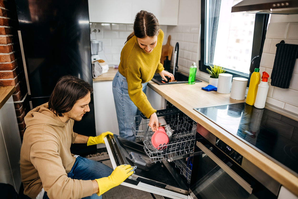 Young couple in yellow gloves showing how to clean a dishwasher