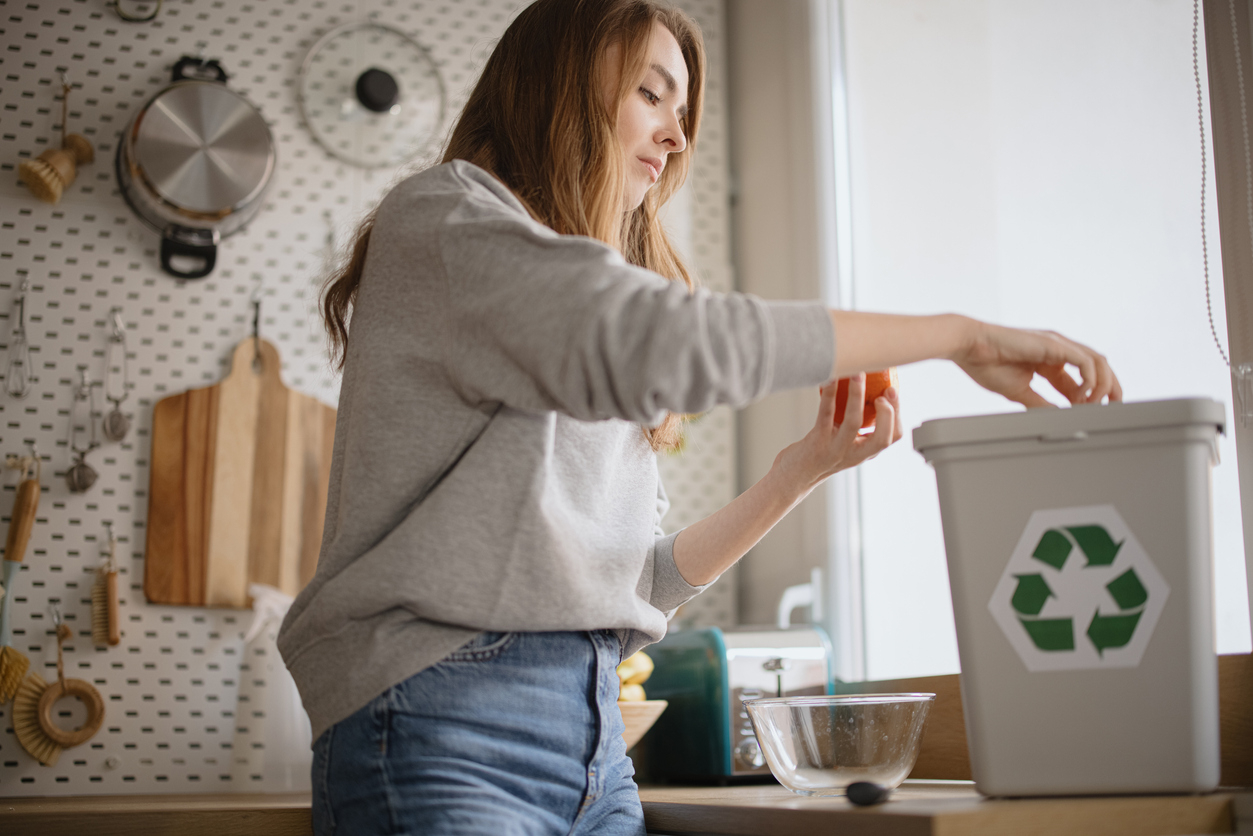 Young woman throwing out rotting fruits to recycle bin to keep fruit flies away