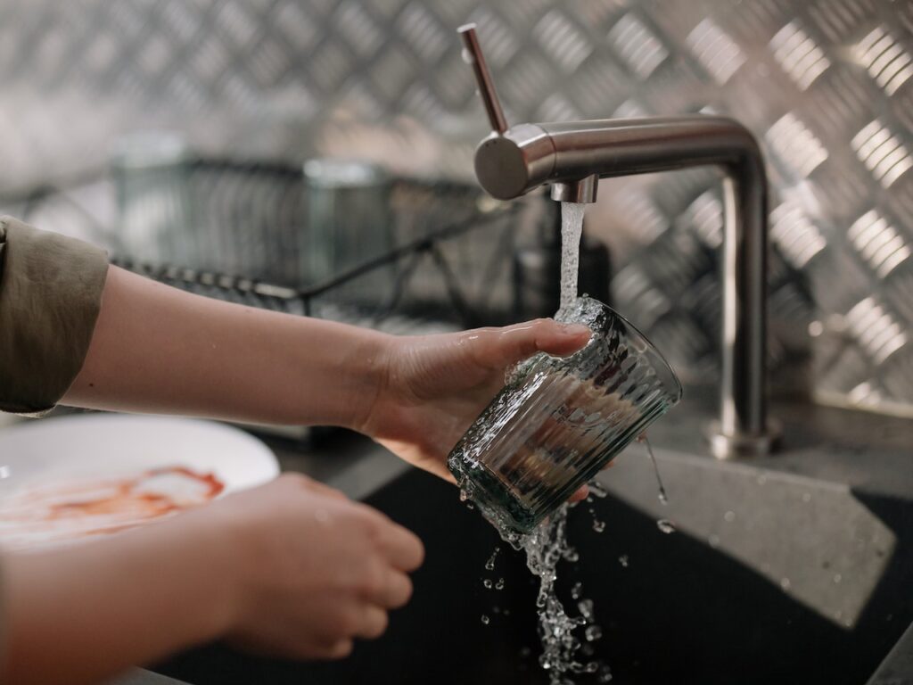 A person pouring water on the drinking glass