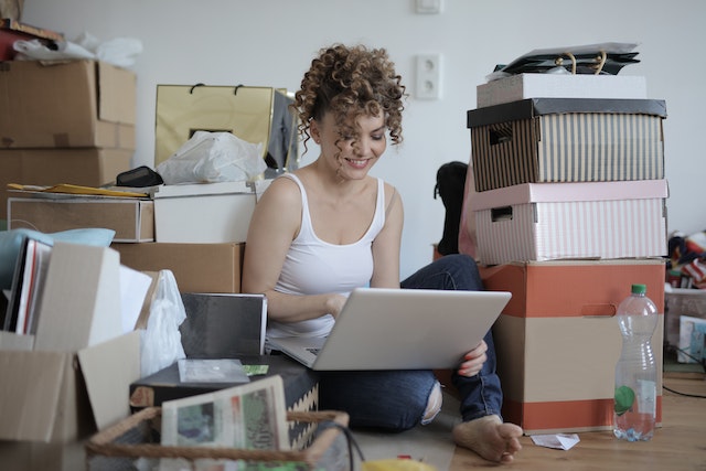 A woman sitting with a laptop on the floor surrounded by boxes