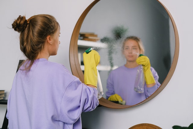 A woman with yellow gloves cleaning the mirror